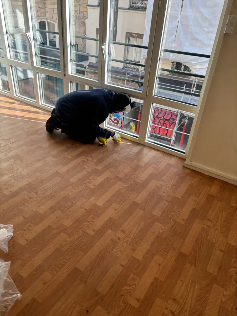 Intervenant accroupi au pied des fenêtres dans une pièce libérée de son mobilier